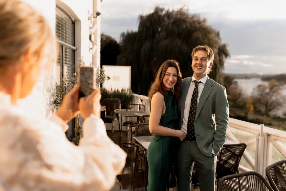 Een stel poseert samen terwijl iemand hen fotografeert op een terras.